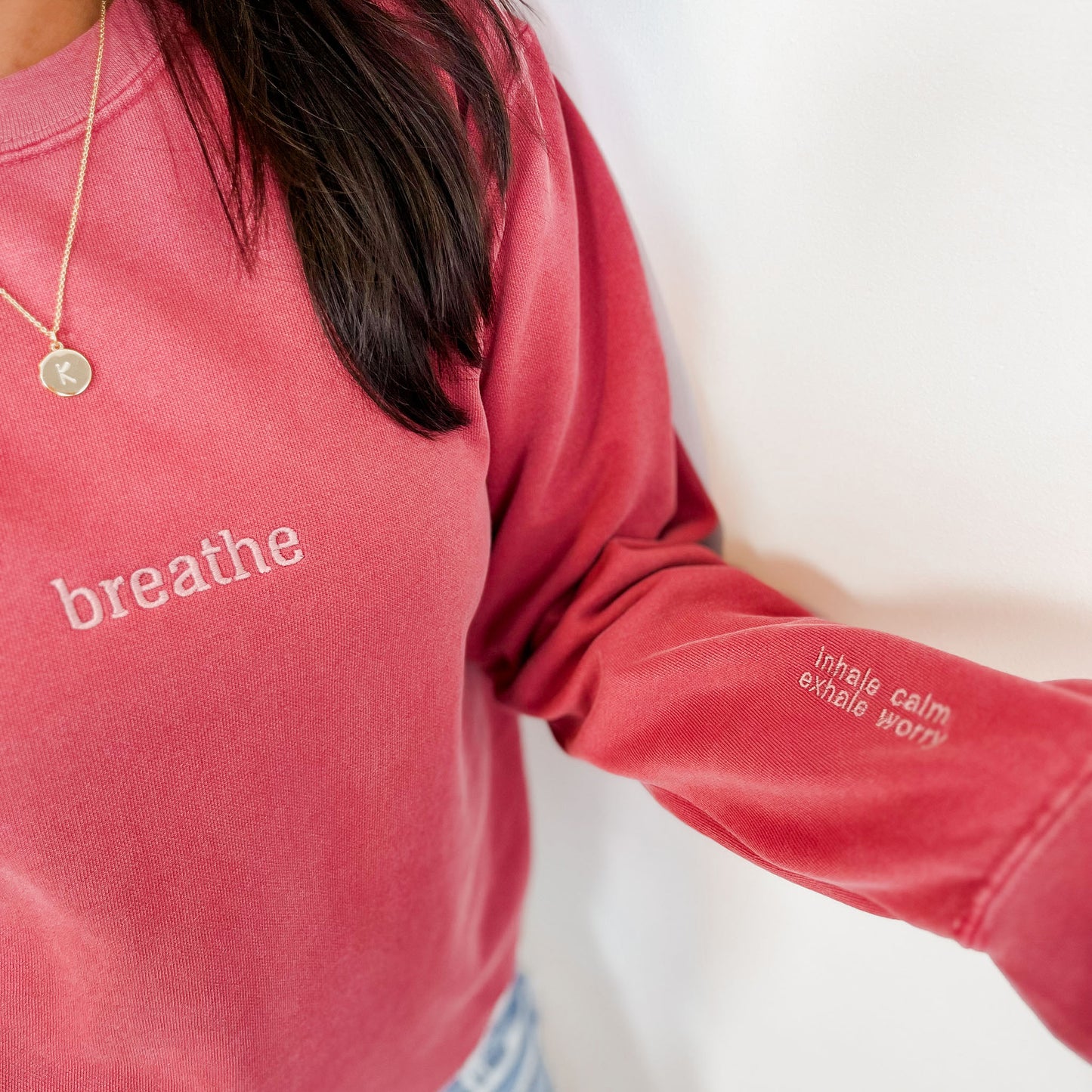 Model is wearing a crimson colour vintage-washed crewneck sweatshirt with the word "breathe" embroidered in a lighter crimson colour.  It is placed in the centre of the chest, 4" below the collar. On the bottom left sleeve, near the cuff, the embroidered words, "inhale calm exhale worry" are stacked.