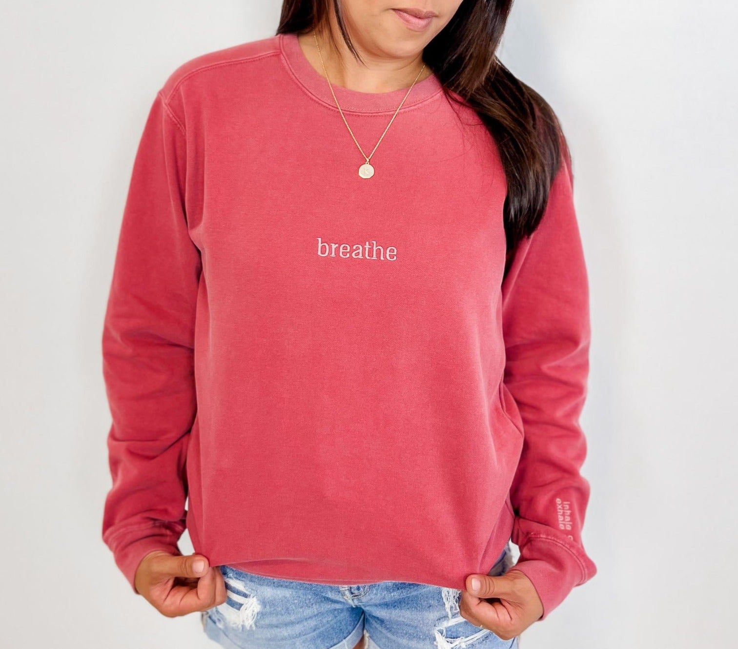 Model is wearing a crimson colour vintage-washed crewneck sweatshirt with the word "breathe" embroidered in a lighter crimson colour.  It is placed in the centre of the chest, 4" below the collar. On the bottom left sleeve, near the cuff, the embroidered words, "inhale calm exhale worry" are stacked.